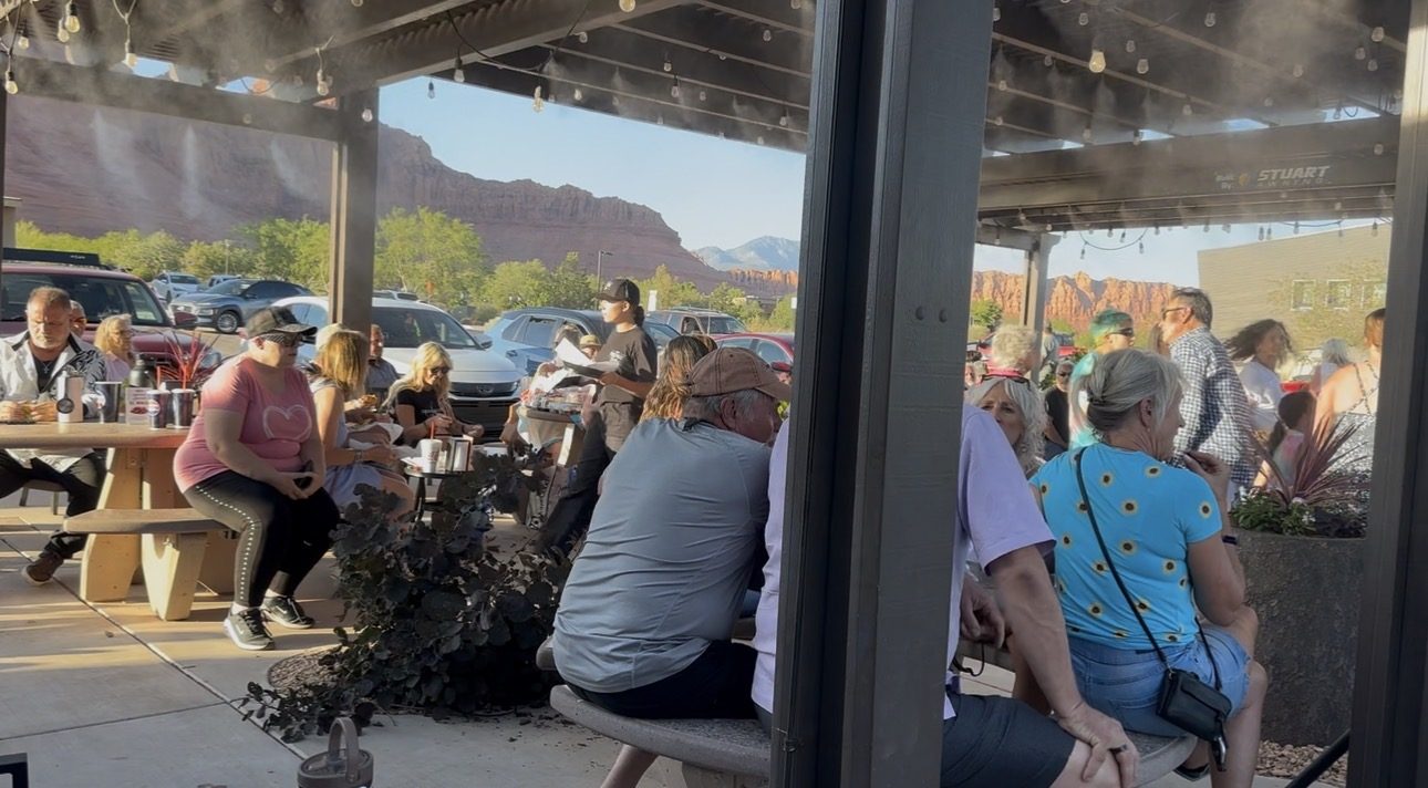 Crowd relaxing at tables under the pergola with mountain views