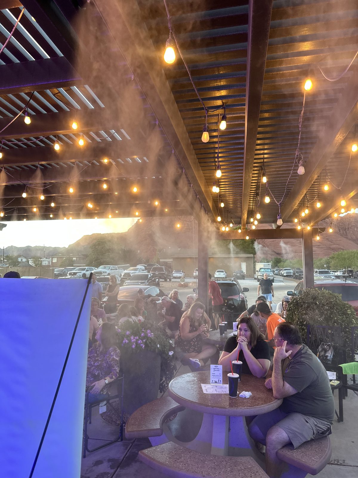 Crowd at tables under the misting fans as the sun sets over the red rocks