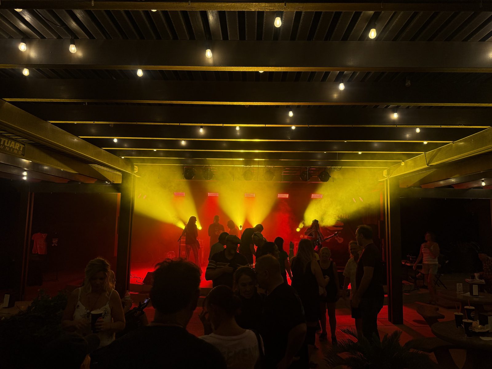 Crowd gathered under the stage lights at a SUMAC show, band performing under red and gold lighting